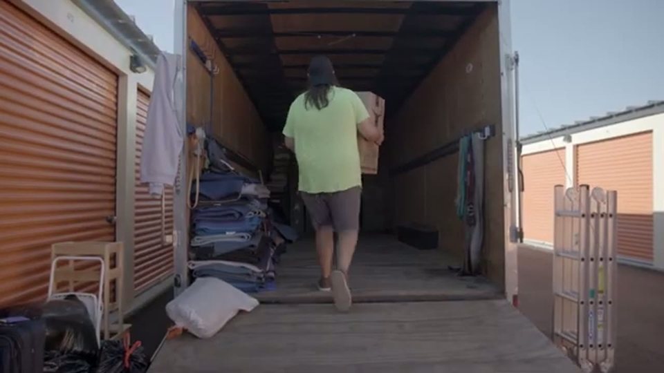 a mover loading a carton into the moving truck outside the storage units