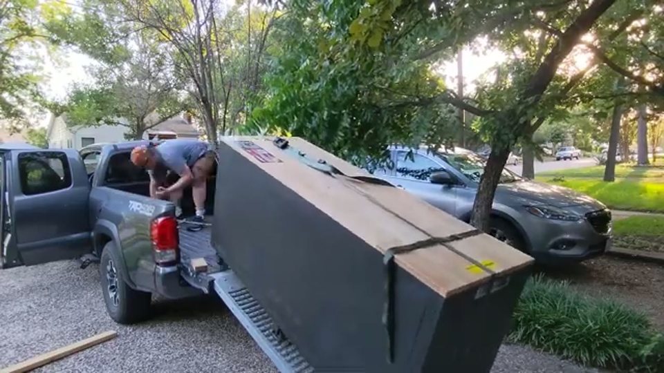 two movers loading a shrink-wrapped dresser onto a pickup truck